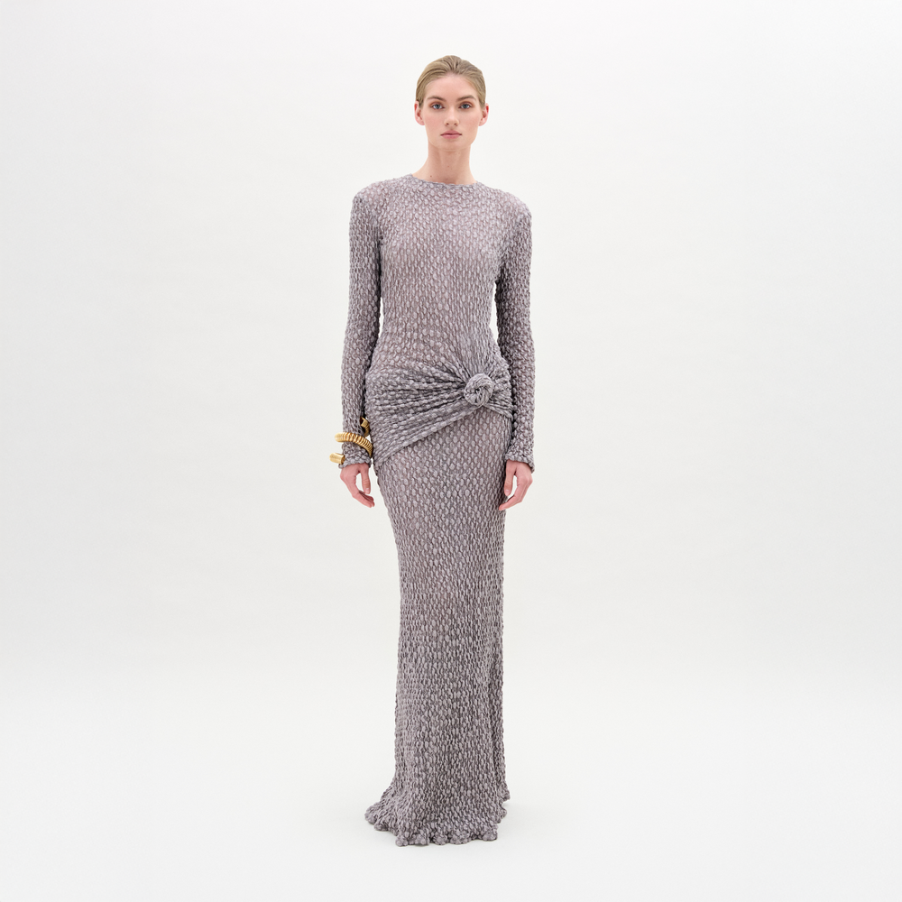 A person faces forward wearing the Ciji Skirt in silver-gray Italian fabric with a textured finish, long sleeves, and a gathered waist, styled with gold bracelets against a white background.