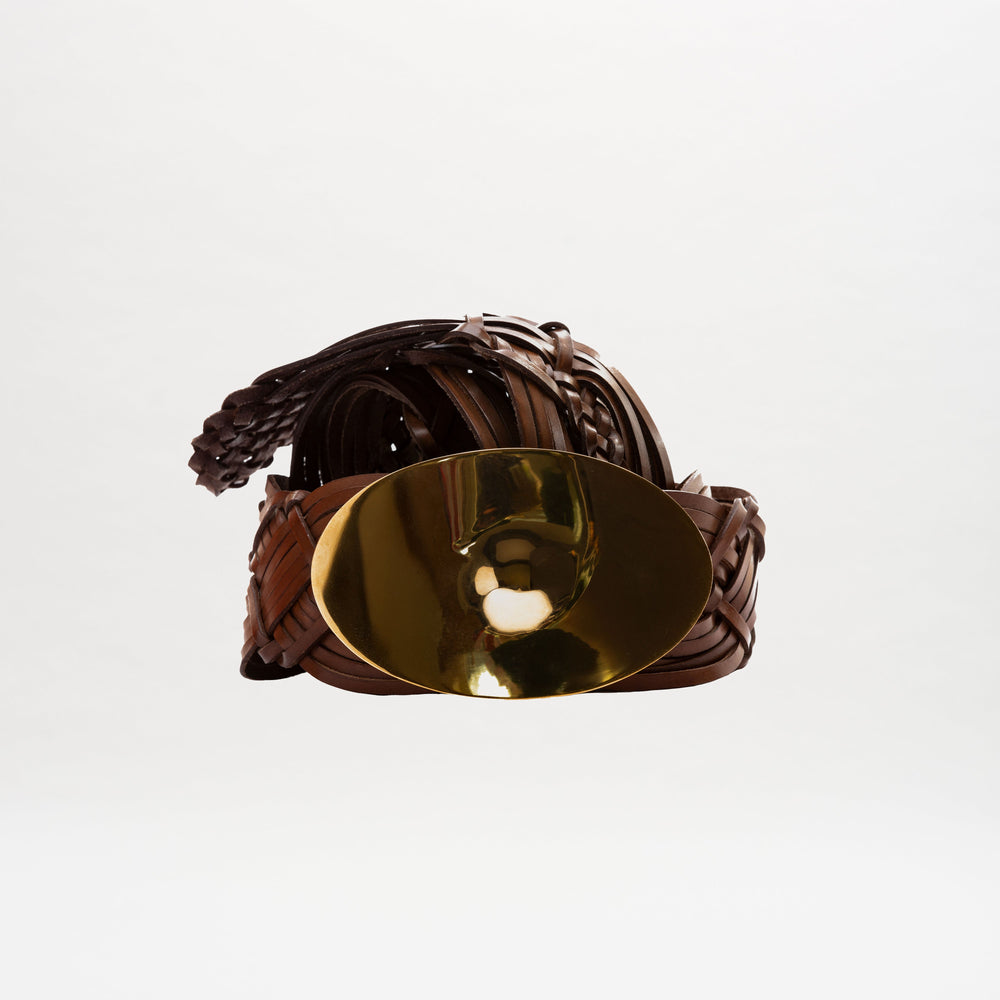 The Clarissa Belt, featuring brown braided leather and a large shiny gold buckle, is displayed coiled on a plain white background.