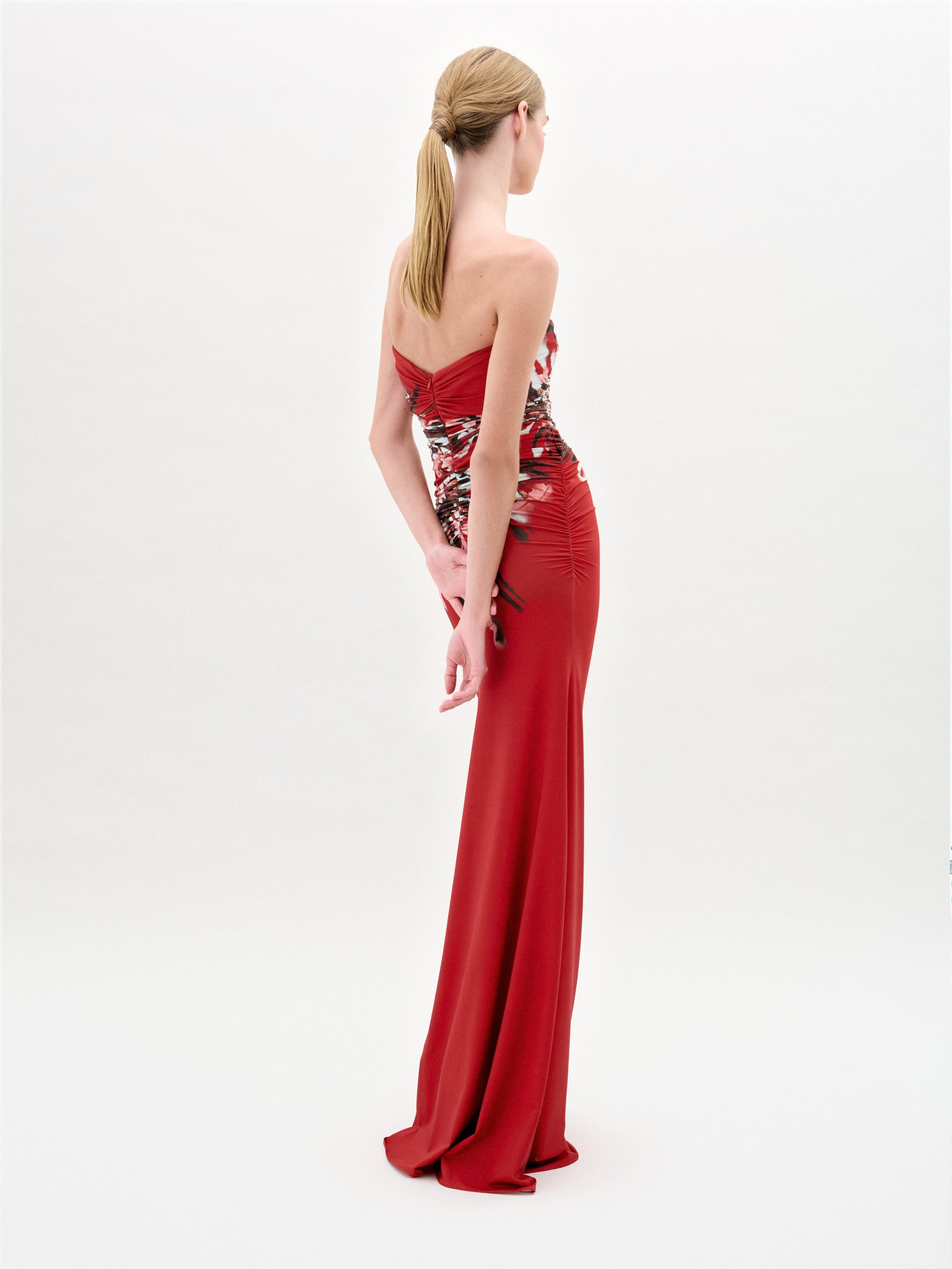A woman wears the Collins Dress, a strapless maxi made from Italian fabric, with a fitted bodice and abstract white, pink, and black floral patterns on the skirt and waist.