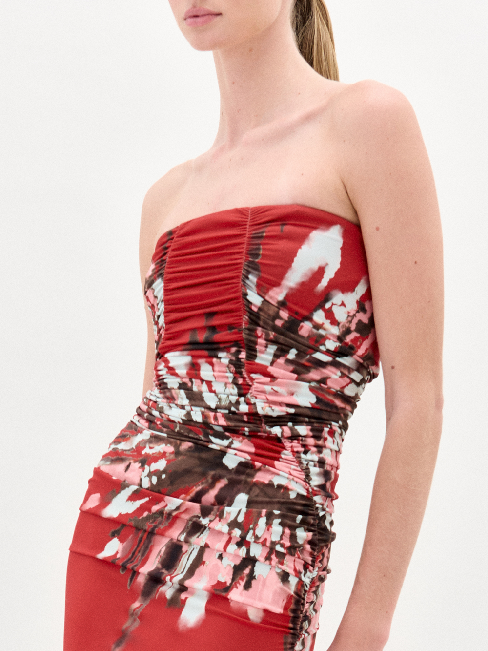 A woman wears the Collins Dress, a strapless maxi made from Italian fabric, with a fitted bodice and abstract white, pink, and black floral patterns on the skirt and waist.