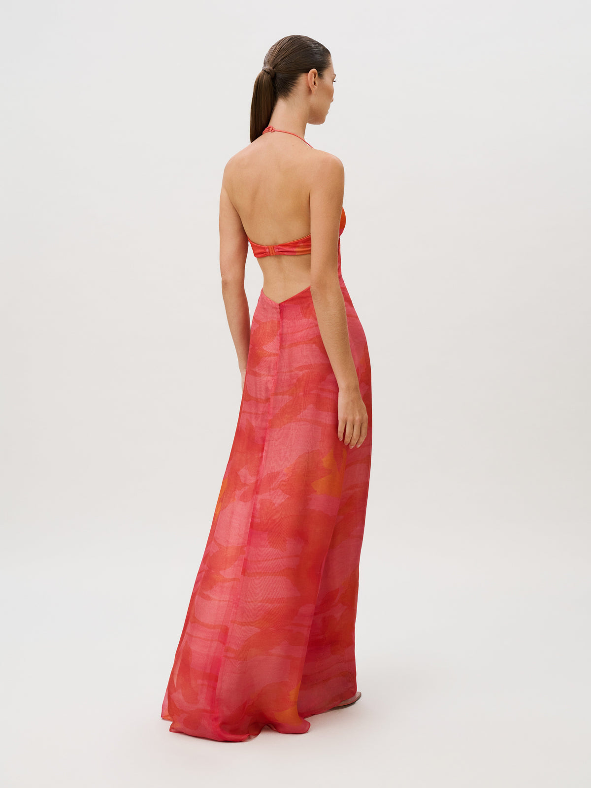 Back view of the Candida Dress, a slim fit, floor-length, backless halter dress in Italian fabric with an orange and pink abstract pattern.
