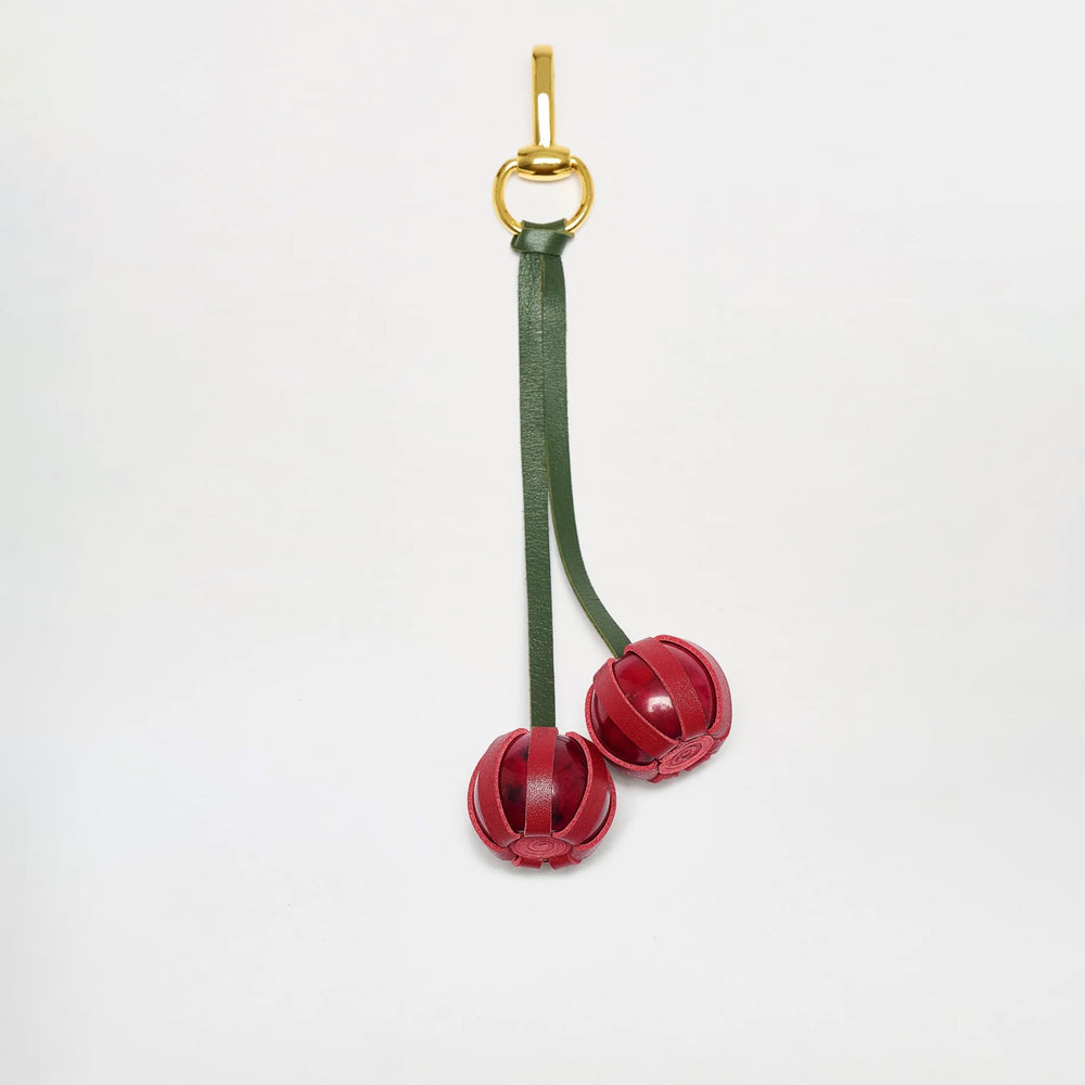 The Candy Charm keyring features green Italian leather straps and two red, spherical leather charms resembling cherries, crafted in Colombia, shown against a plain white background.