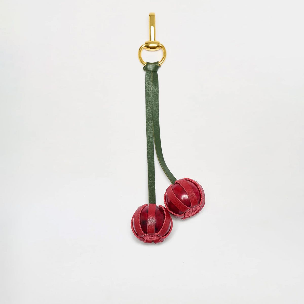 The Candy Charm keyring features green Italian leather straps and two red, spherical leather charms resembling cherries, crafted in Colombia, shown against a plain white background.