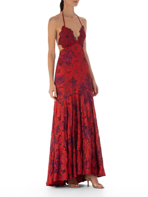 The woman is elegantly dressed in the Cara Dress Red Magenta Embroidery, a floral halter neck maxi dress with an exquisite scalloped guipure lace neckline, standing gracefully against a white background.