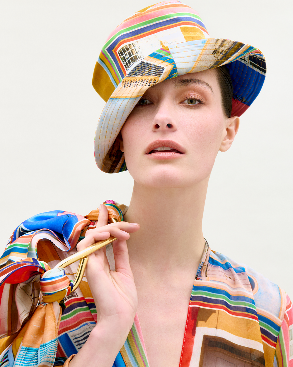 Model wearing a colorful hat and blouse with abstract Cartagena-inspired graphics on a white background, holding a matching patterned bag