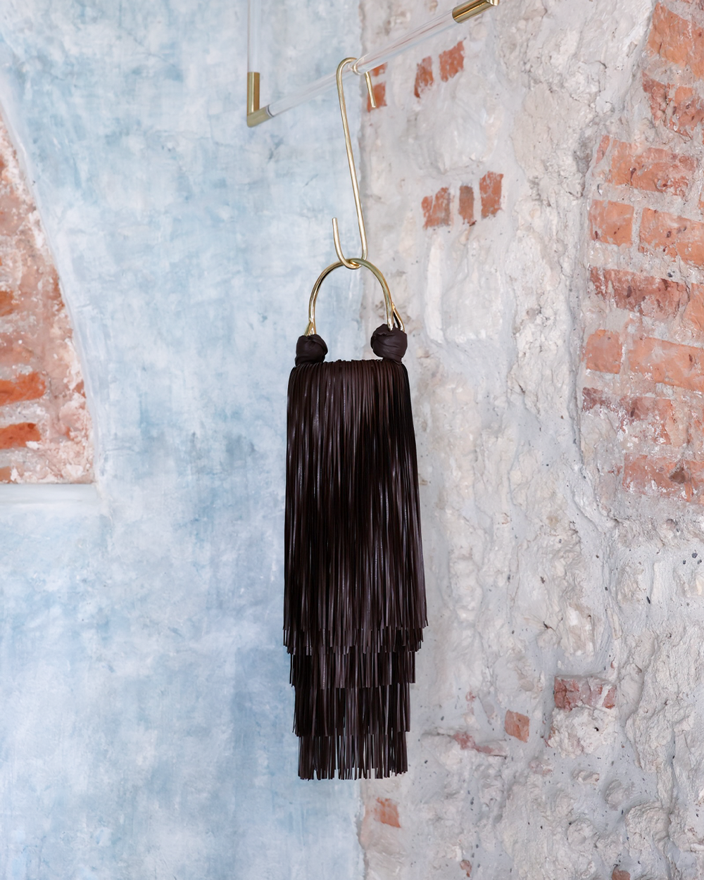 Black handbag tassel earring hanging against a textured wall with brick accents