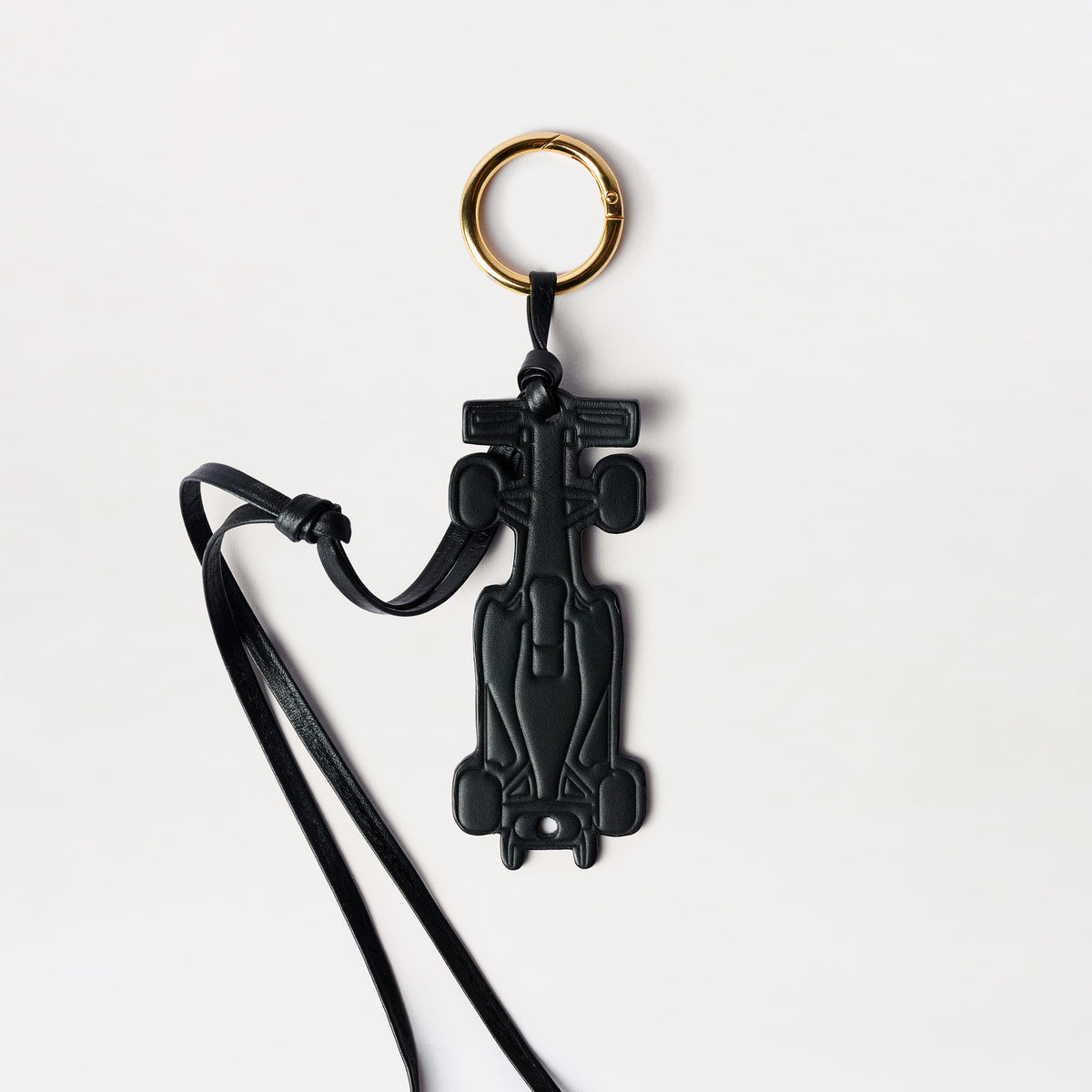 Race Charm: a black Formula 1 race car-shaped keychain featuring a gold-tone ring and an Italian leather strap, displayed on a white background.