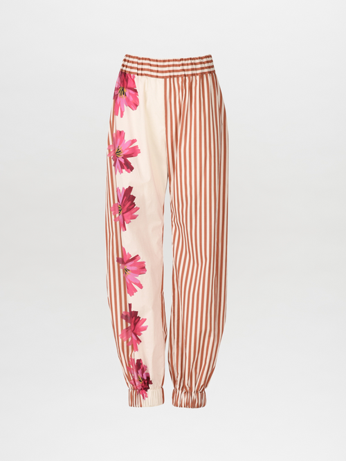 The Chilean Pant Magenta Floral Brushstroke Stripes features light-colored fabric with brown vertical stripes and a magenta floral design on one side. It also comes with an elastic waistband and cuffs for casual luxury.