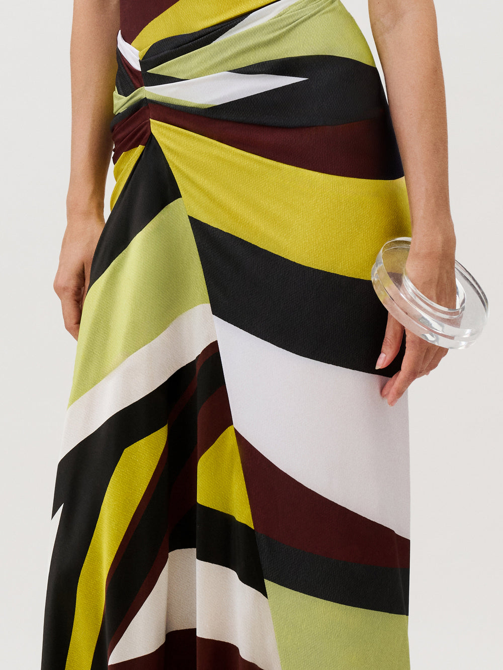 The Claudia Skirt is a slim-fit midi skirt in Italian fabric featuring a black, white, burgundy, and lime green geometric pattern with a gathered waist, styled with a thick clear acrylic bangle.