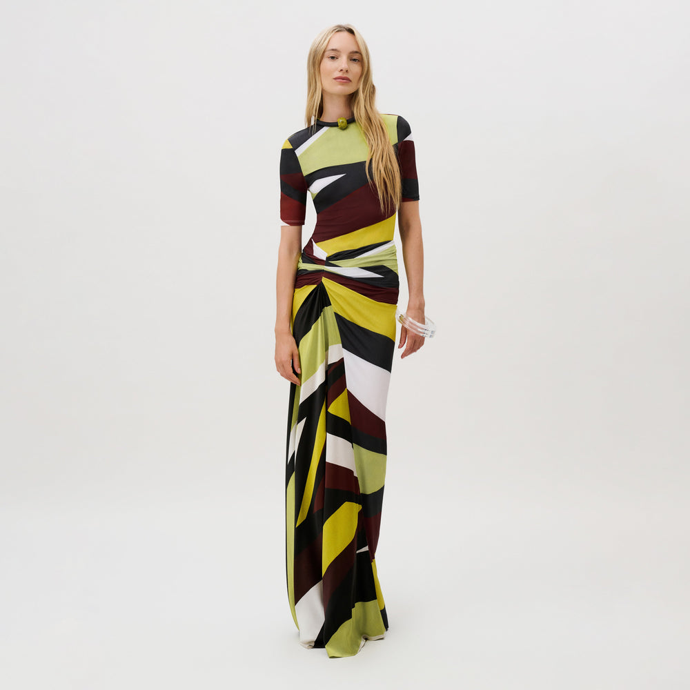 A model wears the Claudia Skirt, a floor-length, slim-fit skirt in Italian fabric featuring a geometric, multicolored abstract print and a gathered, draped waist detail.