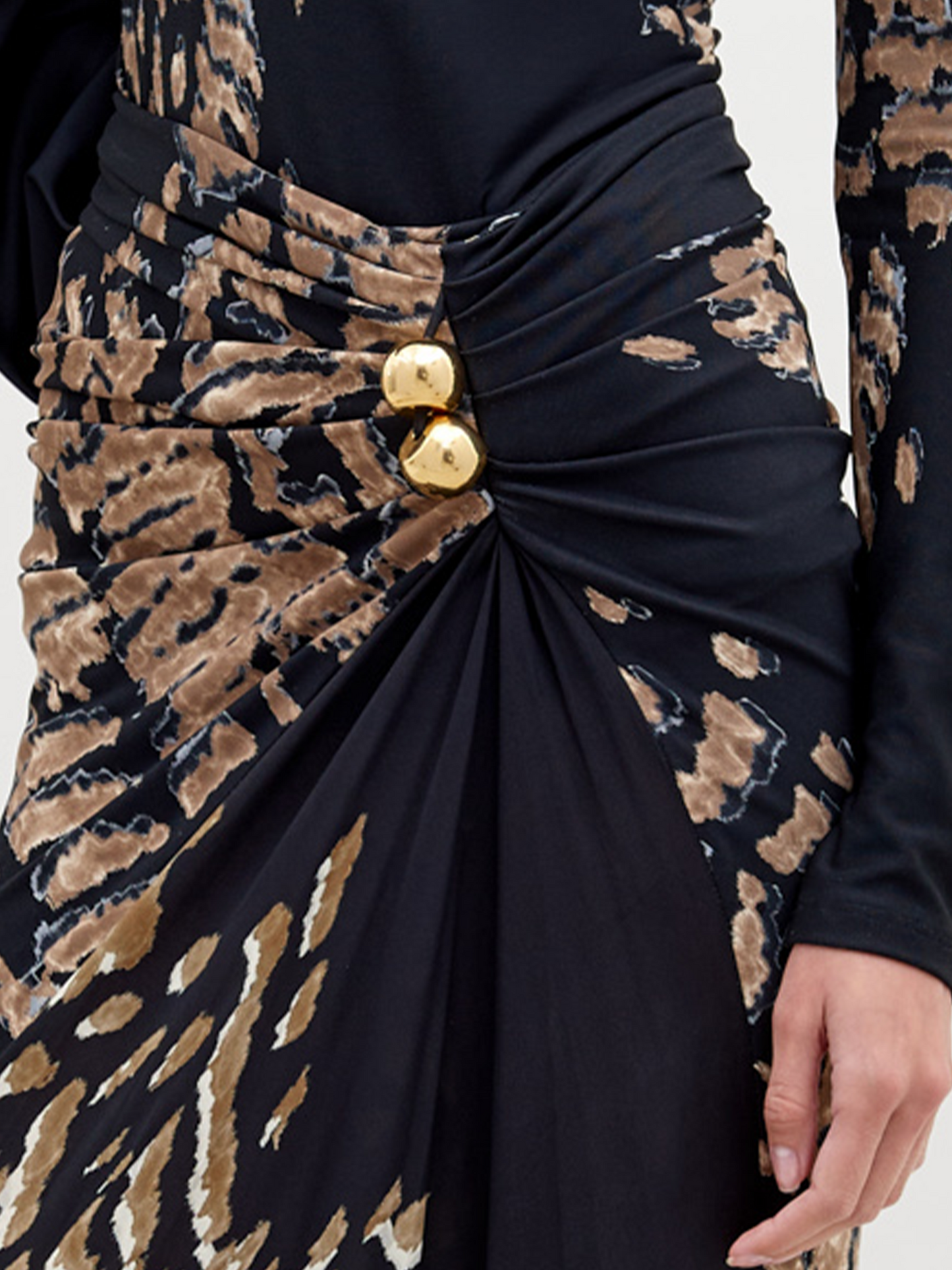 A woman stands wearing a long, fitted Claudia Skirt Black Abstract Animal Print. She has her hair pulled back and is accessorized with a gold necklace. Pre-order now to ensure delivery by the ship date of November 15th, 2024. The background is plain white.