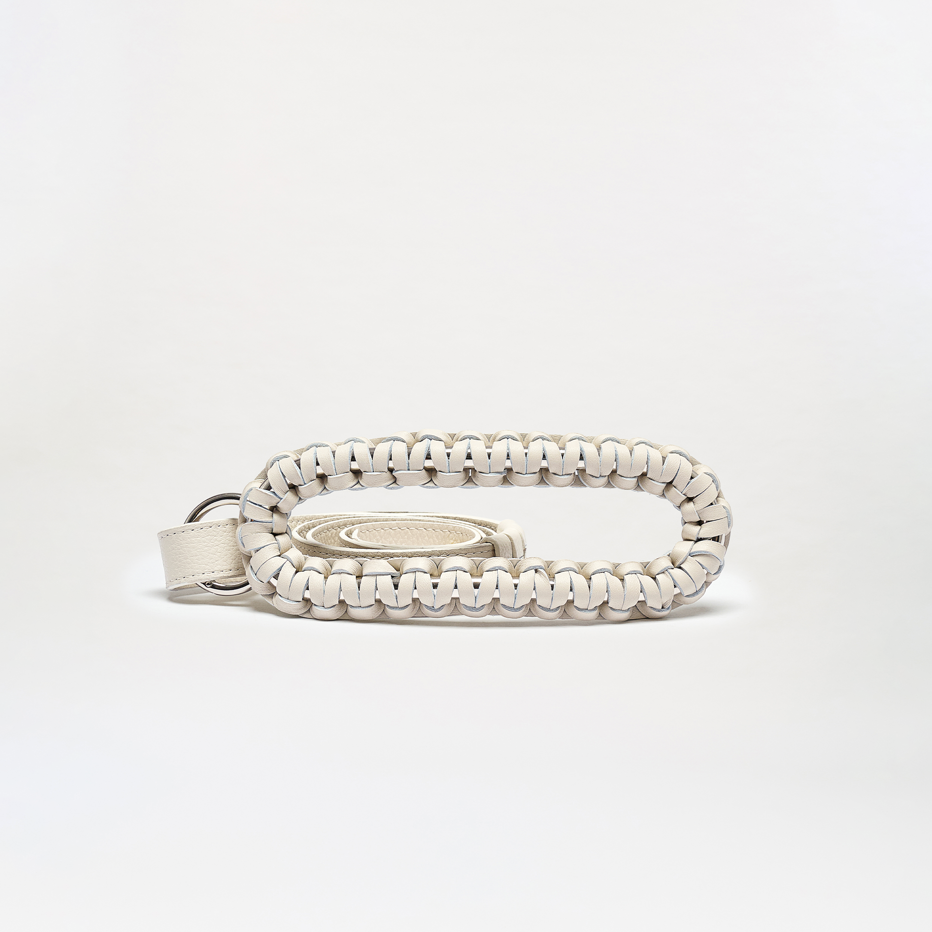 The Cloris Belt is a small, oval-shaped bag made in Colombia from braided white leather with black accents. It features an open center holding a matching coiled strap, and is shown on a plain white background.