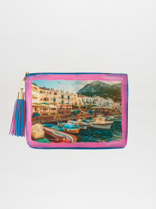 Introducing the Clutch Capri Barcos, a vibrant and limited edition accessory featuring an exquisite image of a coastal town adorned with Swarovski crystals. This clutch showcases beautiful depictions of boats and buildings and is completed with a charming tassel zipper pull. It's the perfect way to infuse your outfit with the boutique charm of Capri.