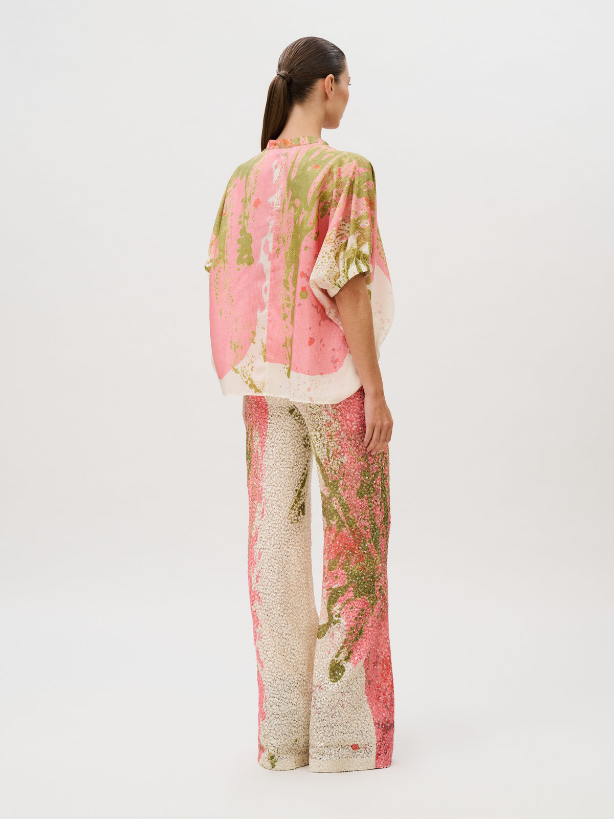 A person seen from the back wearing a loose-fitting short-sleeved top and Como Pant wide-leg Italian fabric trousers, both featuring a pink, green, and cream abstract print.