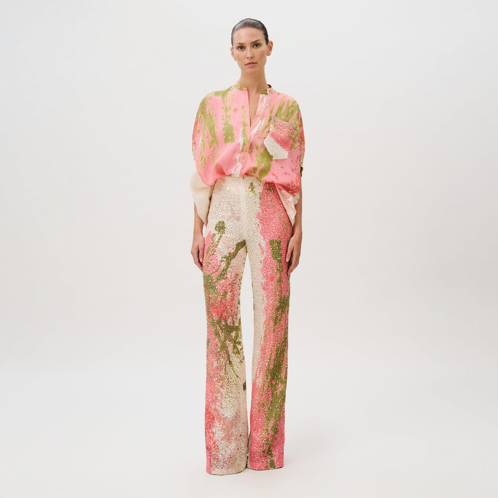 A model wearing a pink and green abstract-print blouse and matching Como Pant wide-leg sequin trousers made in Colombia.