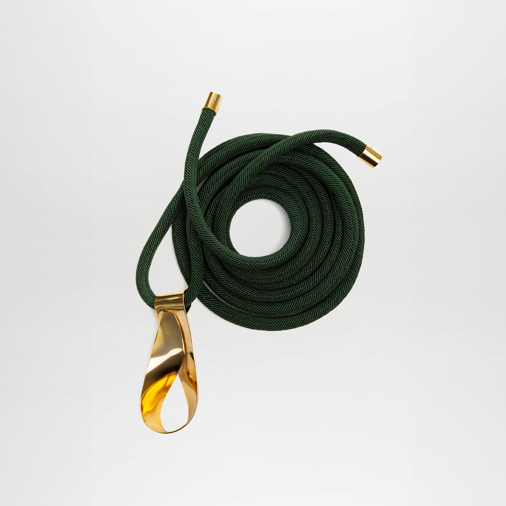 The Daiana Belt is a coiled dark green cord with gold metal caps and a large gold-plated brass buckle, crafted from fine Italian material and shown on a plain white background.