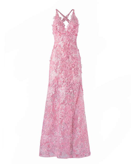 A person stands wearing the Daira Dress Pink, a long dress with thin straps and a beautiful floral pattern. The background is plain and light-colored. This elegant dress is now available for pre-order and will ship by February 1st, 2025.