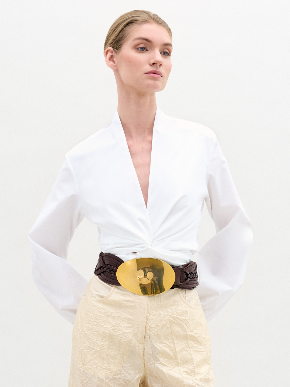 The Dania Blouse is a white long-sleeve top featuring a deep V-neck and twist knot detail at the front waist.