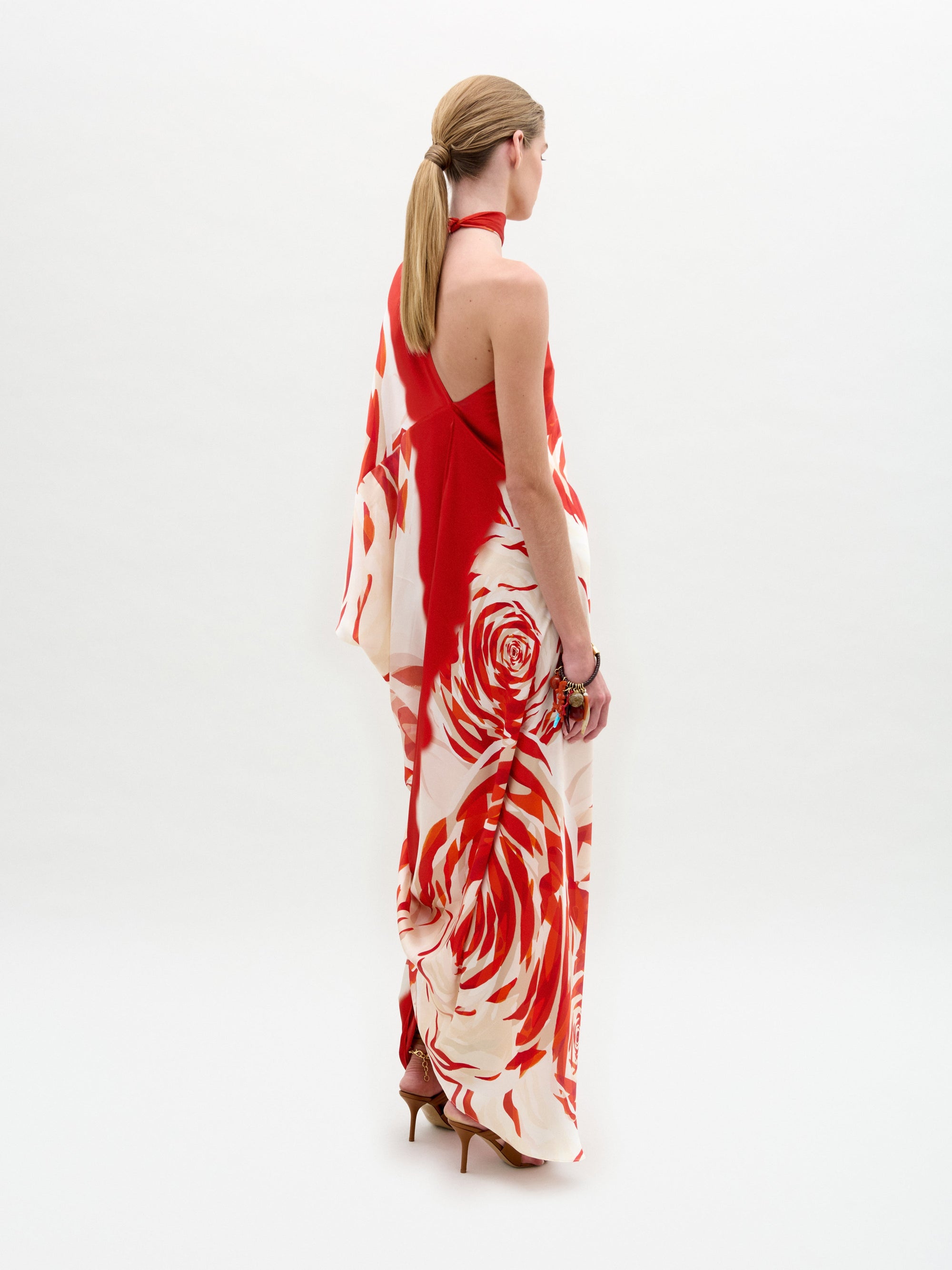 Woman standing in a Dani Tunic—red and white floral one-shoulder silk maxi dress with high heels and side slit—against a plain white background.