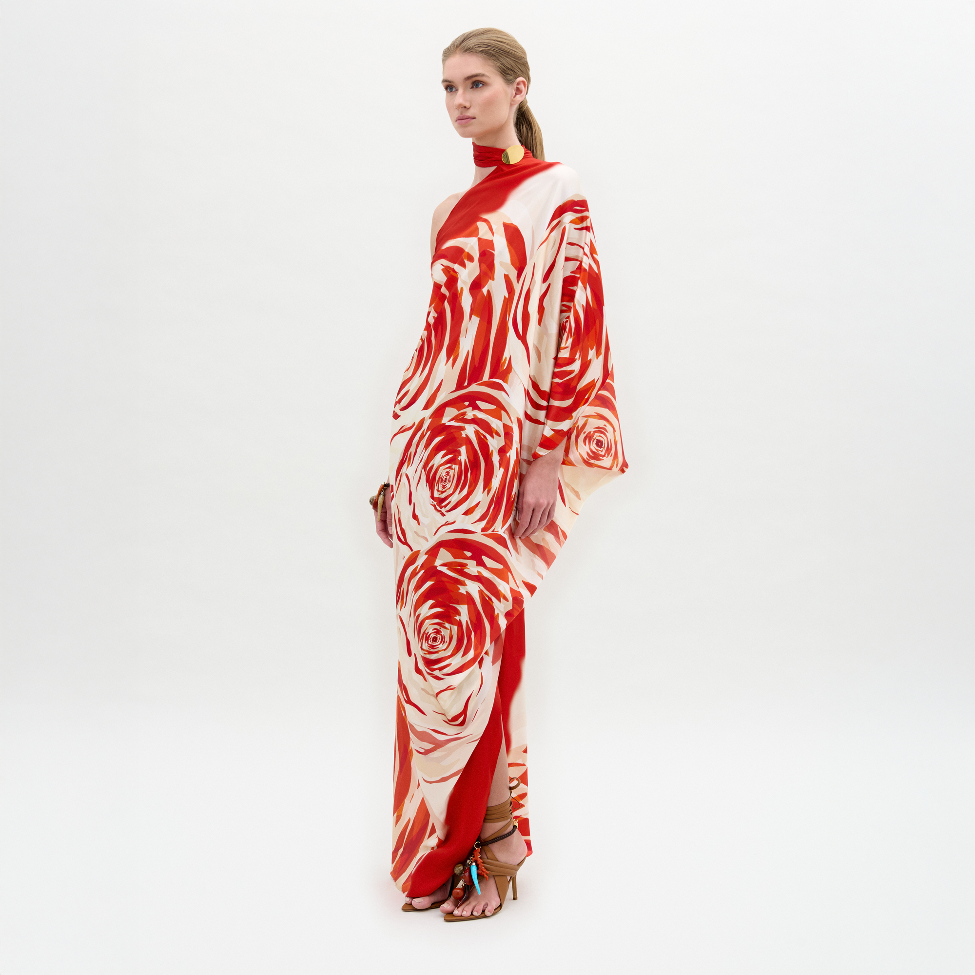 Woman standing in a Dani Tunic—red and white floral one-shoulder silk maxi dress with high heels and side slit—against a plain white background.