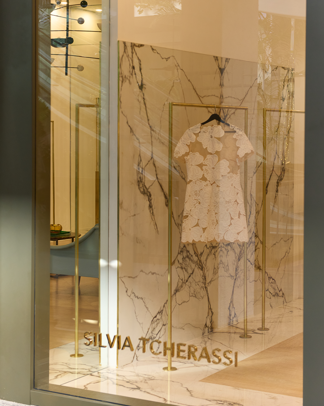 Display window featuring a white lace dress with floral patterns, hung against a marble background. The name Silvia Tcherassi is visible at the bottom.