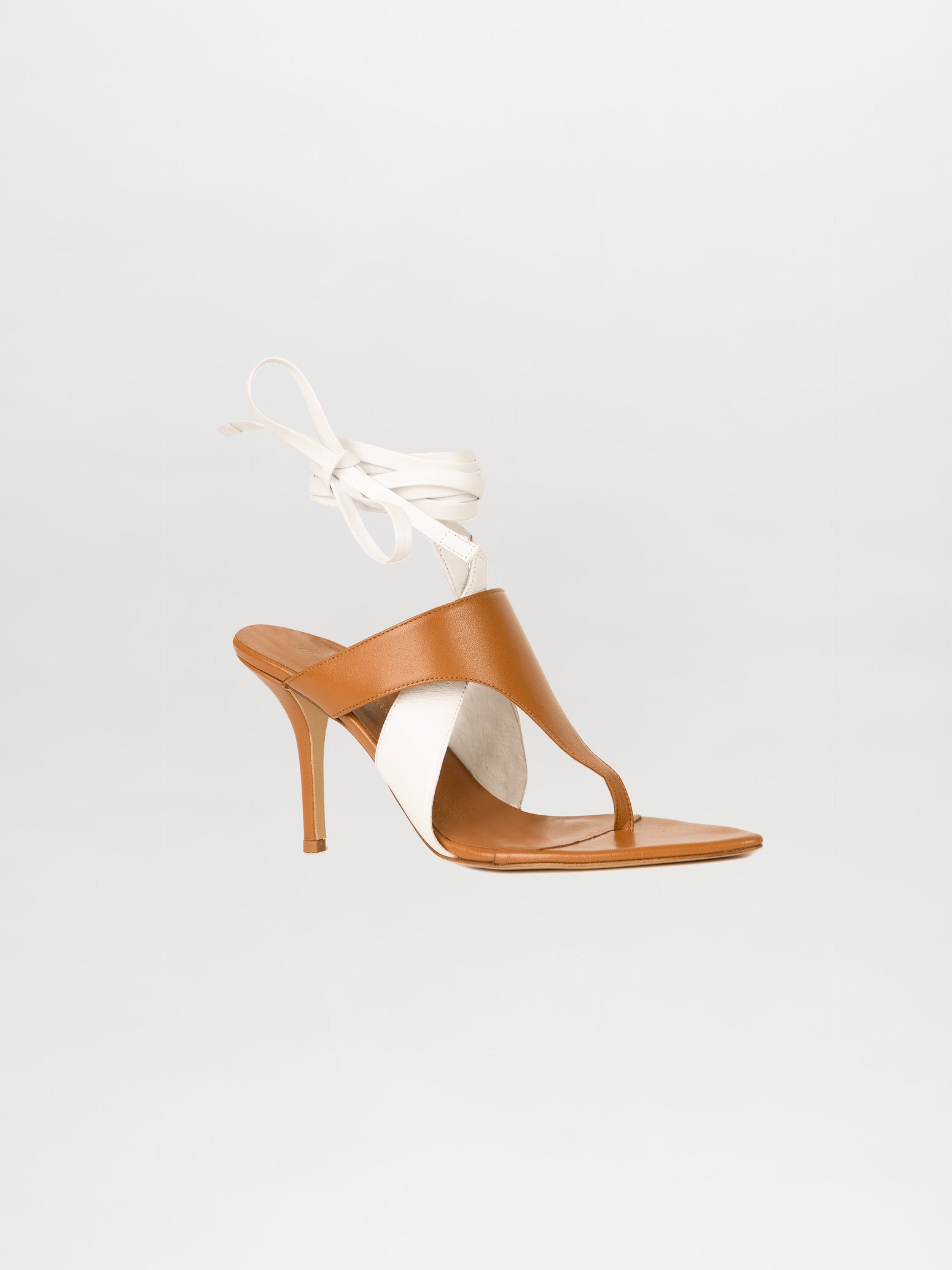 The Domenico Heels in Beige/White are crafted from luxurious Italian leather, featuring a brown and white high-heeled sandal design with an elegant ankle wrap strap, set against a plain background.