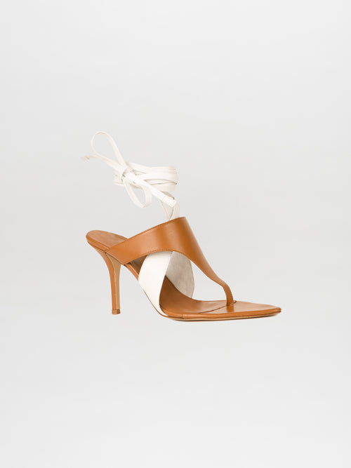 The Domenico Heels in Beige/White are crafted from luxurious Italian leather, featuring a brown and white high-heeled sandal design with an elegant ankle wrap strap, set against a plain background.