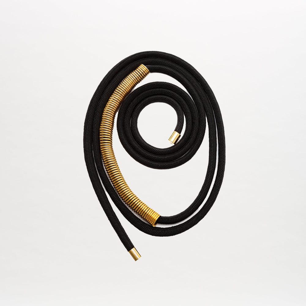The Dunia Belt, crafted from fine Italian material, features a coiled black cord with gold-capped ends and striking gold accents, artfully arranged in a spiral on a plain white background.