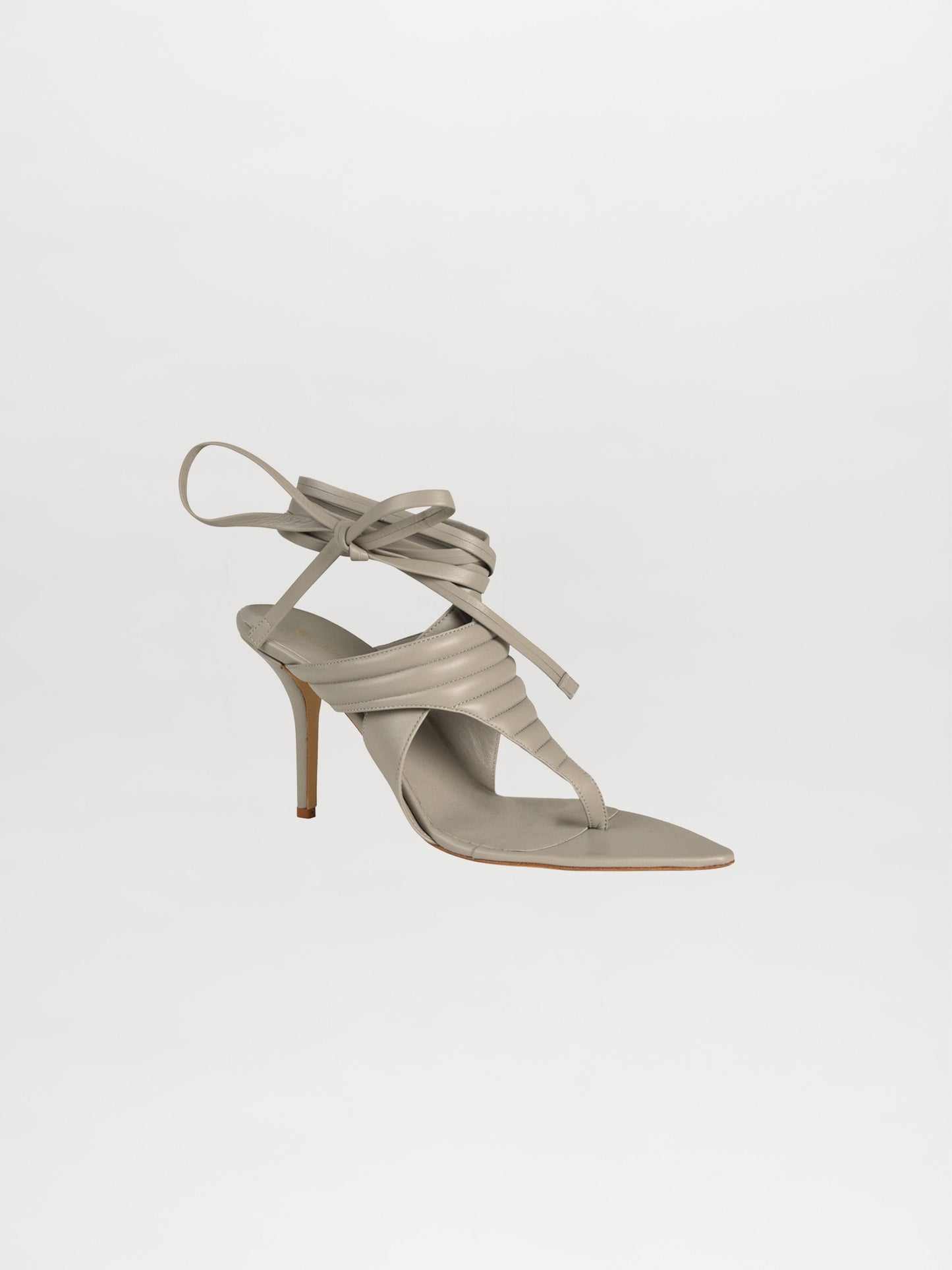 The Dalila Heels Grey are a stunning single strappy high-heeled sandal crafted from Italian calf leather in grey, featuring elegant wraparound ankle straps against a white background.