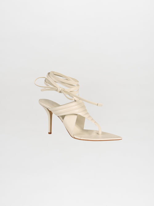 An individual Dalila Heel in off-white, crafted from luxurious Italian calf leather, features elegant wraparound ankle straps and is showcased beautifully against a plain white background.