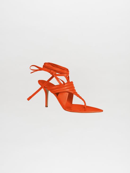 The Dalila Heels Orange showcases an elegant single high-heeled sandal crafted from luxurious Italian calf leather in a vibrant orange hue, featuring a strappy design with ankle ties, all set against a plain white background.