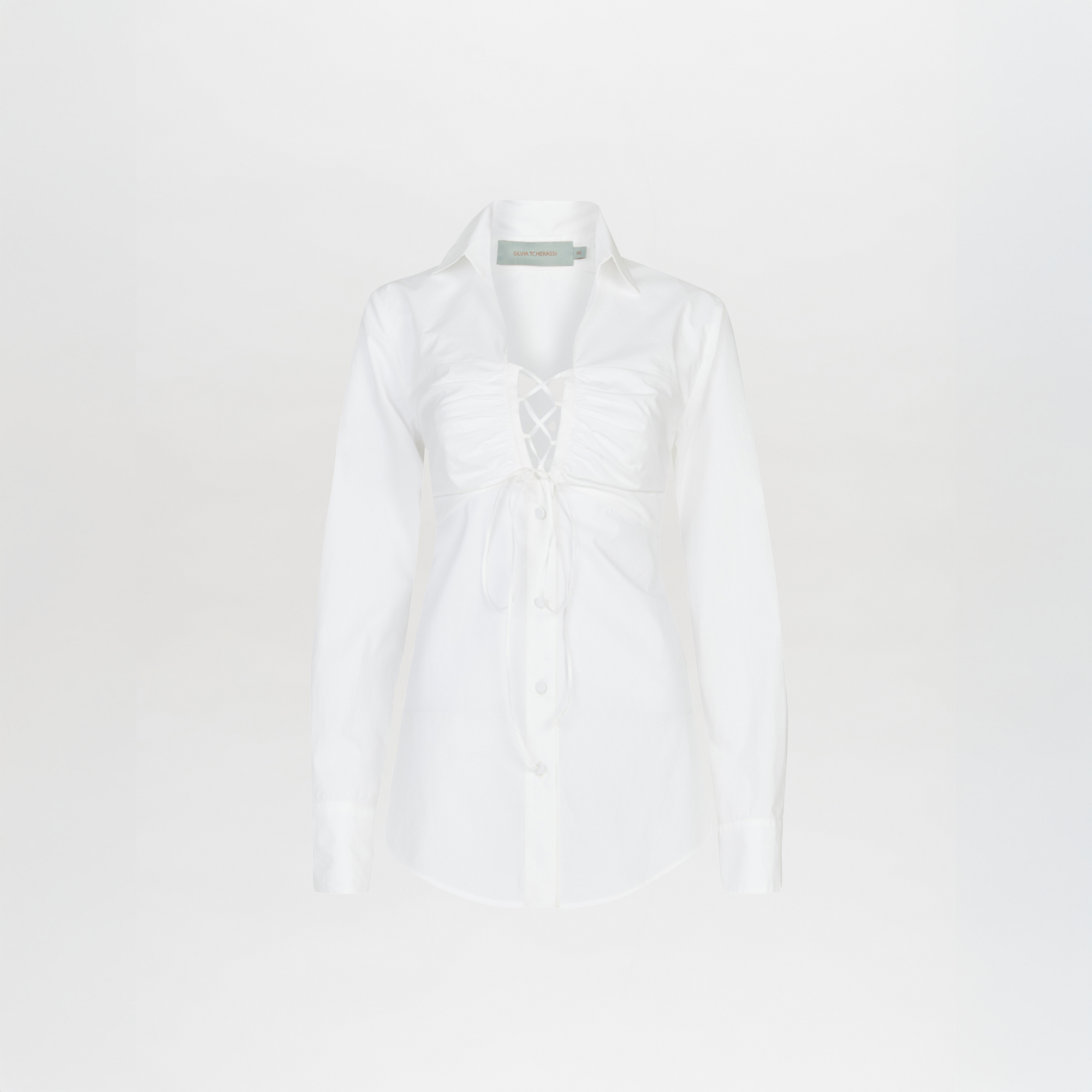 The Dileta Blouse White features crisp cotton, tailored sleeves, a classic collar, and ruched lace-up detail at the chest; shown on a plain white background.
