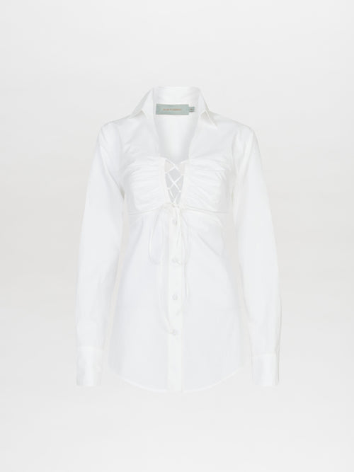 The Dileta Blouse White, crafted from crisp white cotton, features a lace-up front detail, long tailored sleeves, and a collar. It is displayed against a neutral background.