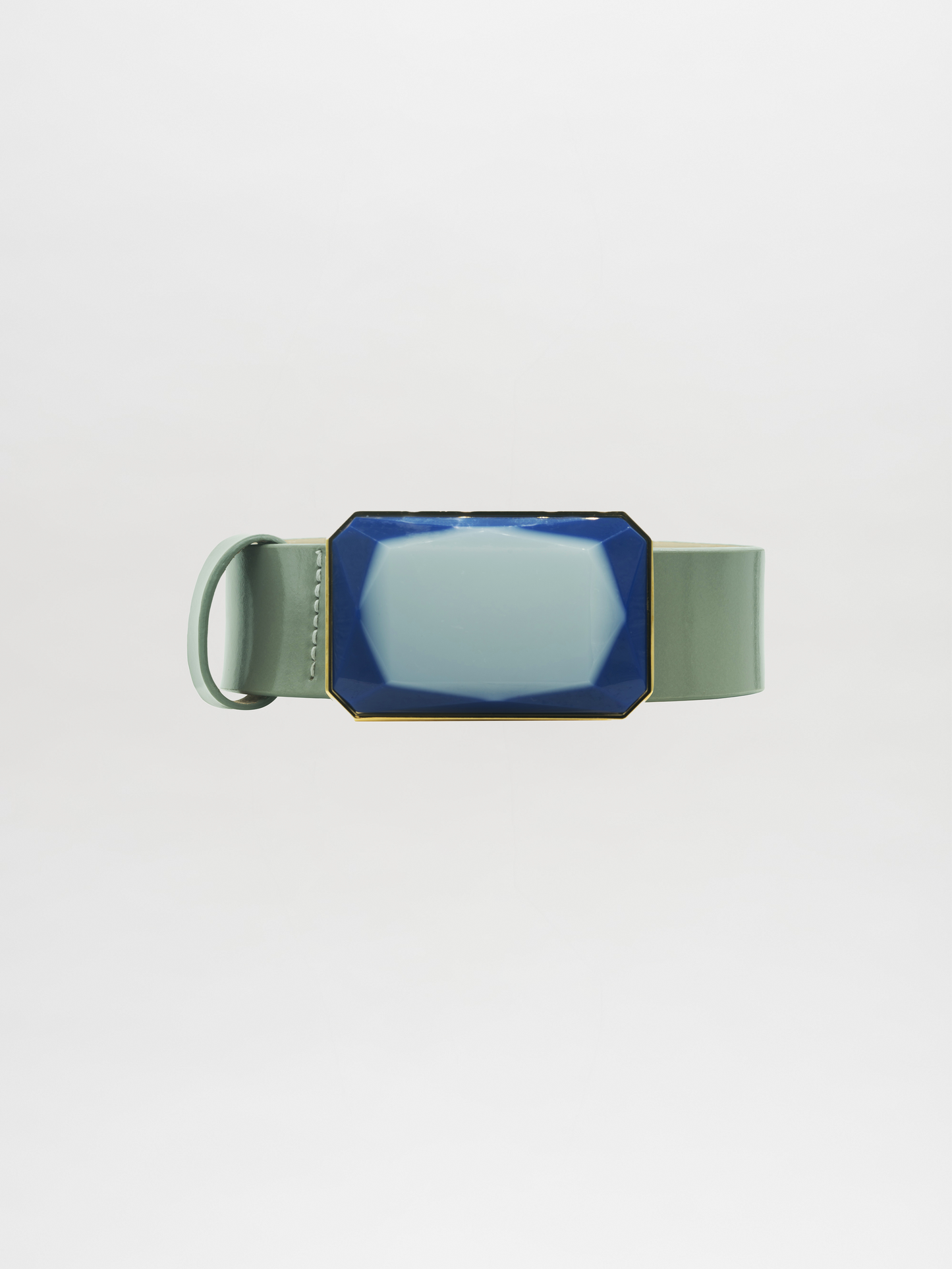 A Dora Belt Steel Blue wristband, featuring a large, faceted blue and gold centerpiece, rests elegantly on a light gray background, ready to ship within days of your order.