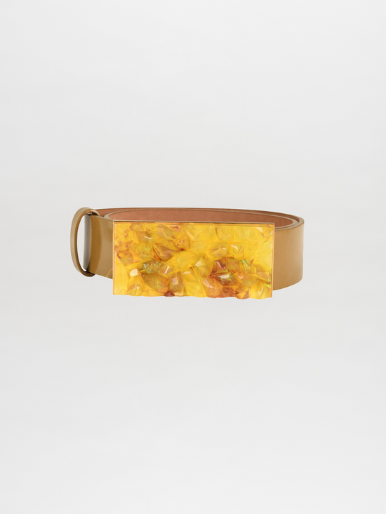 The Dora Belt Mustard in camel leather showcases a sleek, rolled-up design coupled with a large rectangular yellow buckle, reflecting the elegant style synonymous with Silvia Tcherassi.