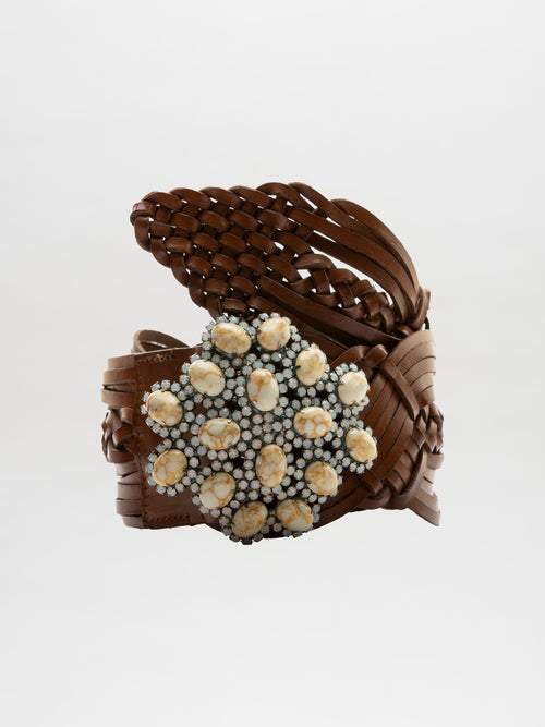 The Eines Belt is a braided brown leather accessory with a large decorative clasp adorned with white and yellow embellishments, crafted from luxurious Italian leather.