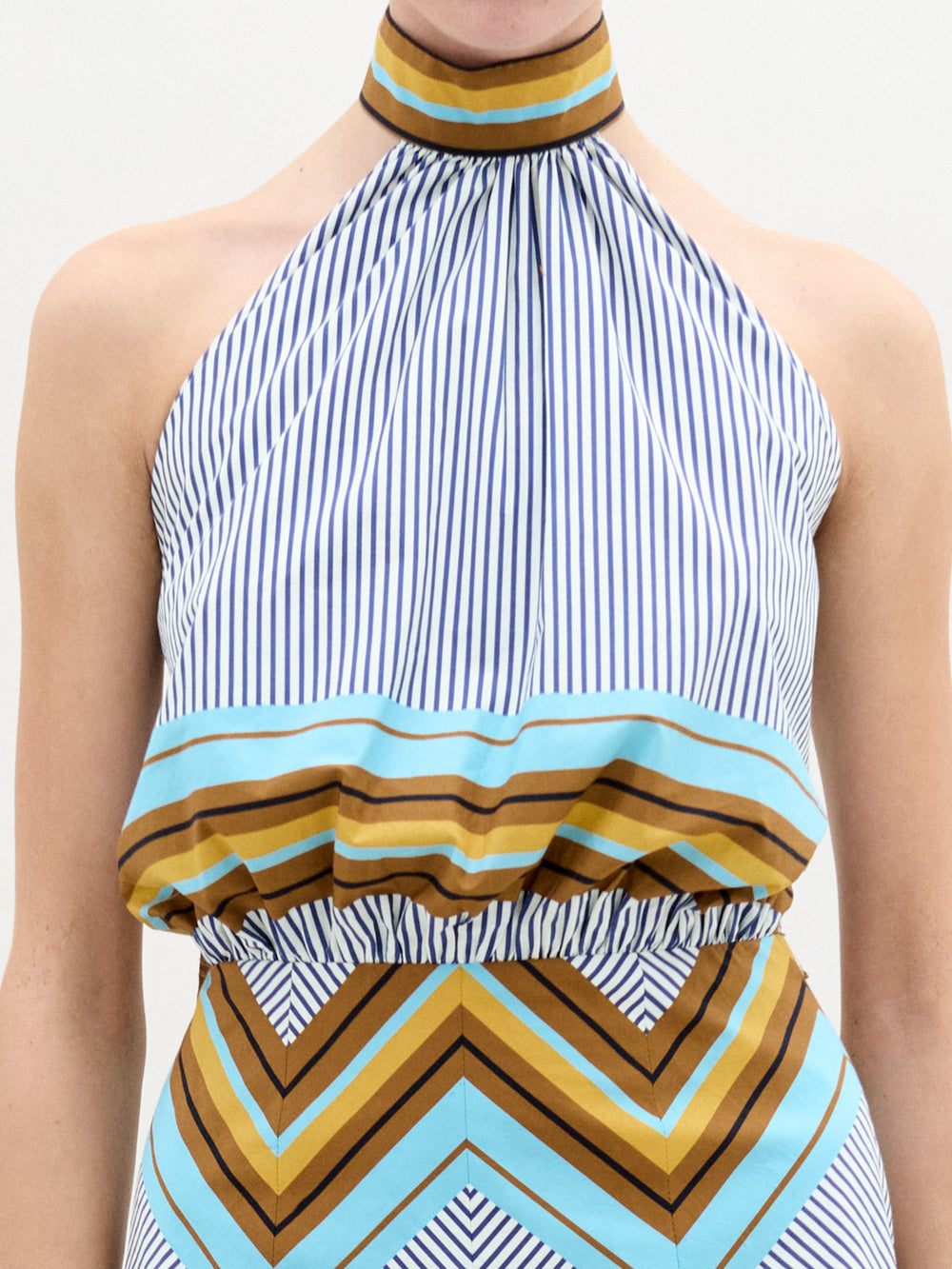 A person faces forward against a plain white background wearing the Elara Dress, a sleeveless, knee-length midi with geometric patterns and an A-line skirt, paired with ankle-strap heels.