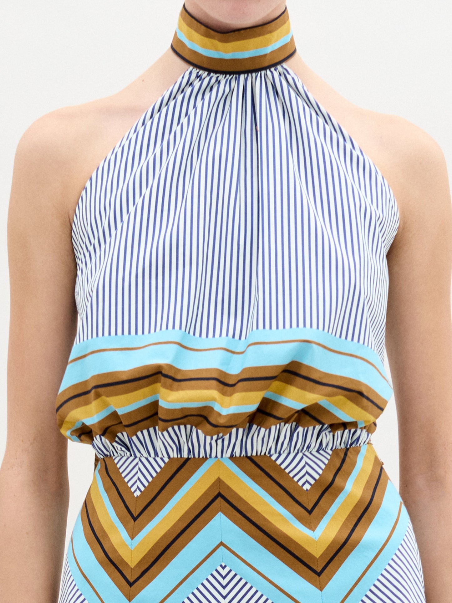 A person faces forward against a plain white background wearing the Elara Dress, a sleeveless, knee-length midi with geometric patterns and an A-line skirt, paired with ankle-strap heels.