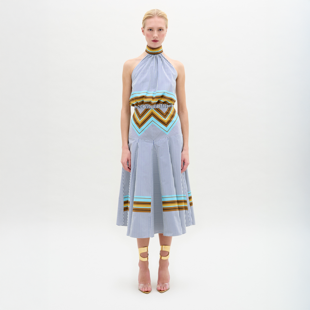 A person faces forward against a plain white background wearing the Elara Dress, a sleeveless, knee-length midi with geometric patterns and an A-line skirt, paired with ankle-strap heels.