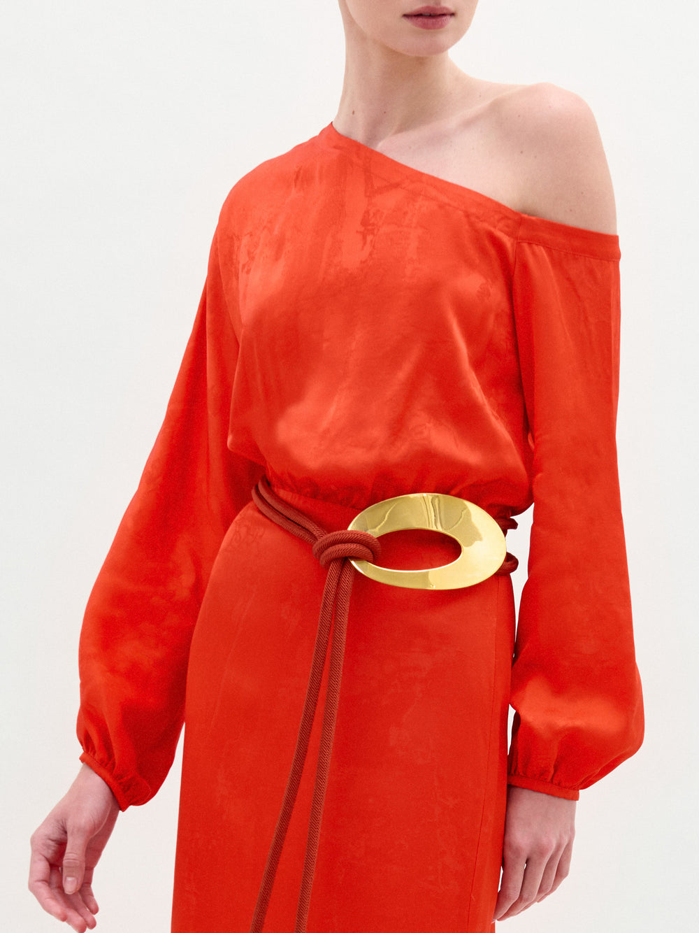 A person wearing the Elga Dress in color Vibrant Orange with a golden Belt on a white background.