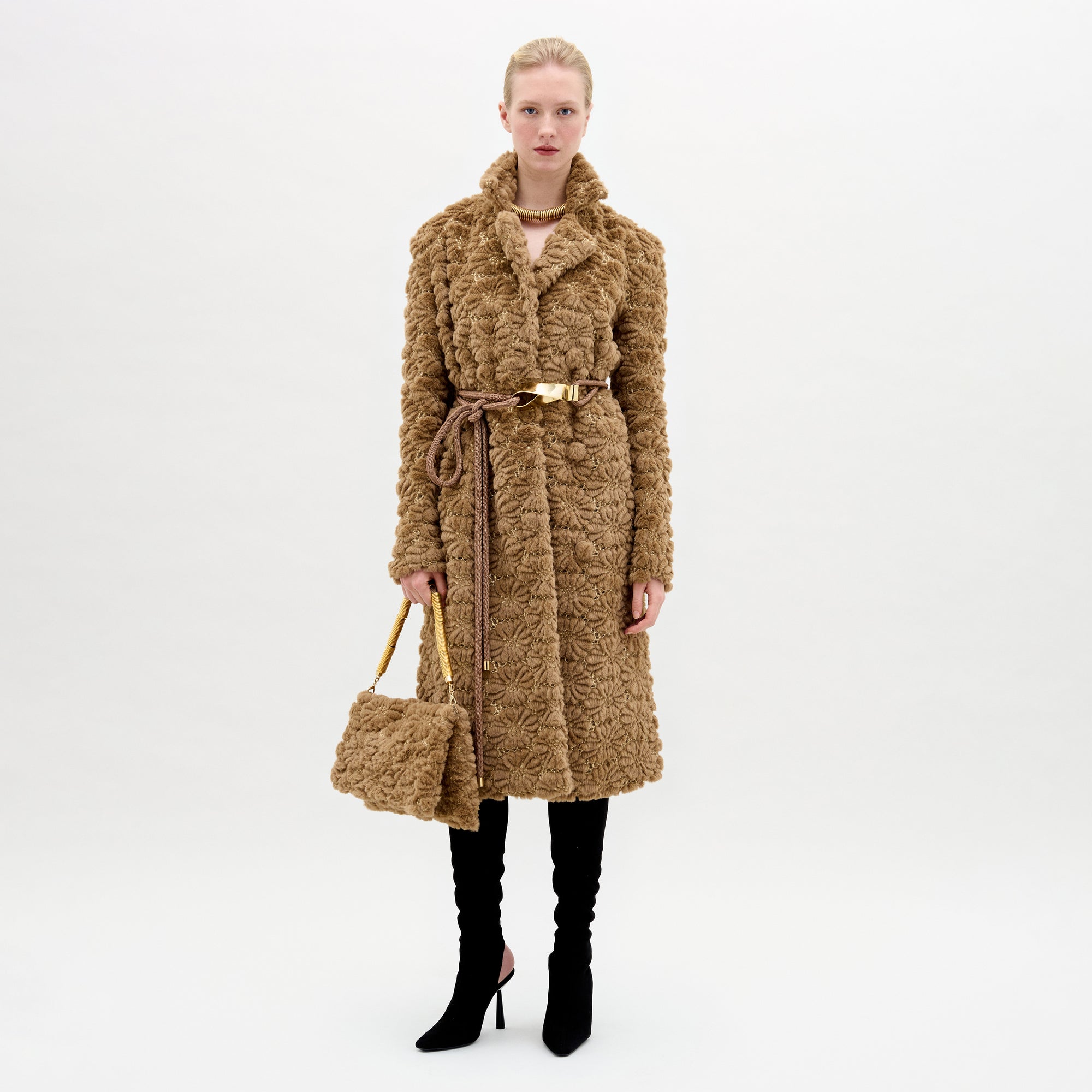 A woman wearing the Emerson Trench in color Camel with a Turni clutch in color Camel on a white background.