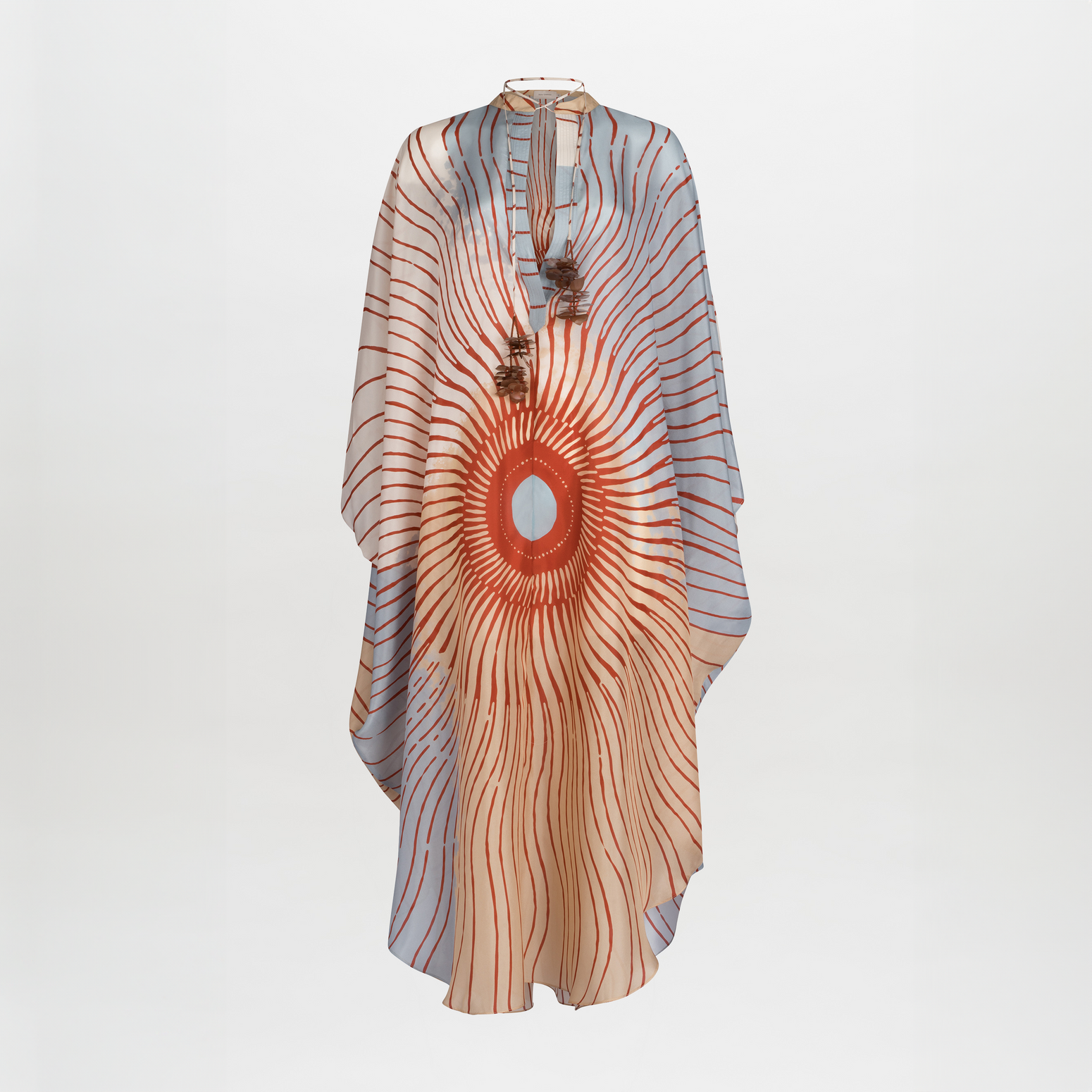 A Elea Tunic Sausalito Sunset with an orange and cream sunburst design, adorned with tassels and a circular centerpiece.