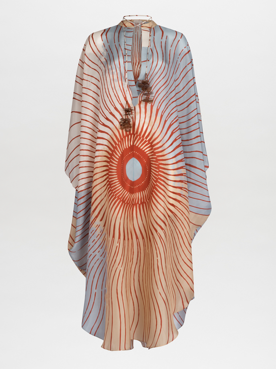 A Elea Tunic Sausalito Sunset with an orange and cream sunburst design, adorned with tassels and a circular centerpiece.