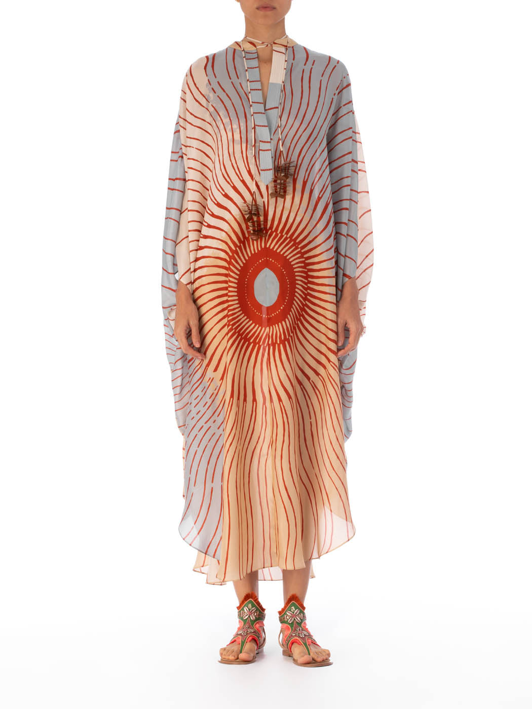 A Elea Tunic Sausalito Sunset with an orange and cream sunburst design, adorned with tassels and a circular centerpiece.