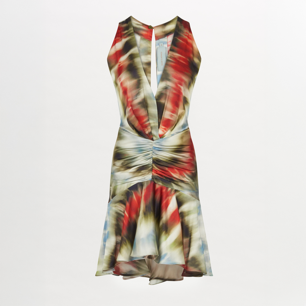 Dressed in the Elettra Dress Multi Linear, which boasts a sleeveless cut with a vibrant multi-linear distortion pattern, deep V-neckline, and ruffled hem, the person stands elegantly against a plain background.