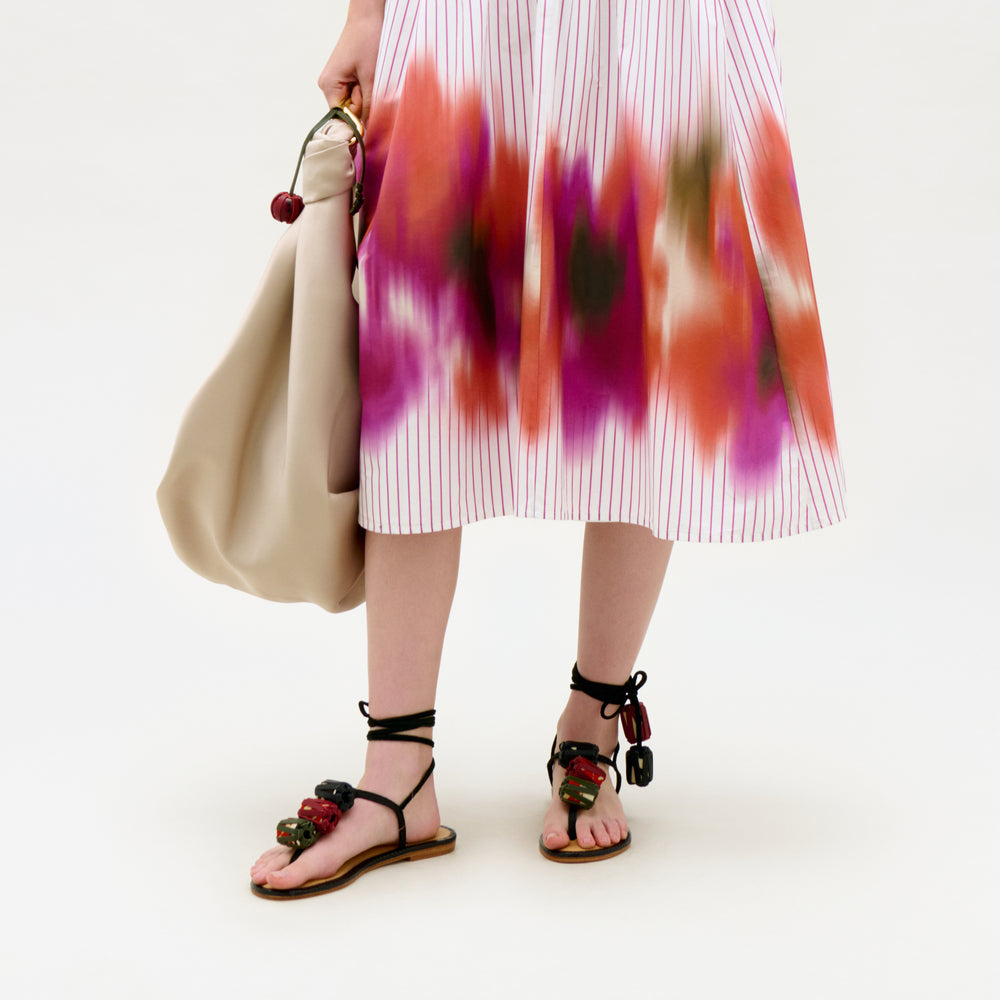 Person wearing a colorful dress with floral sandals on a white background