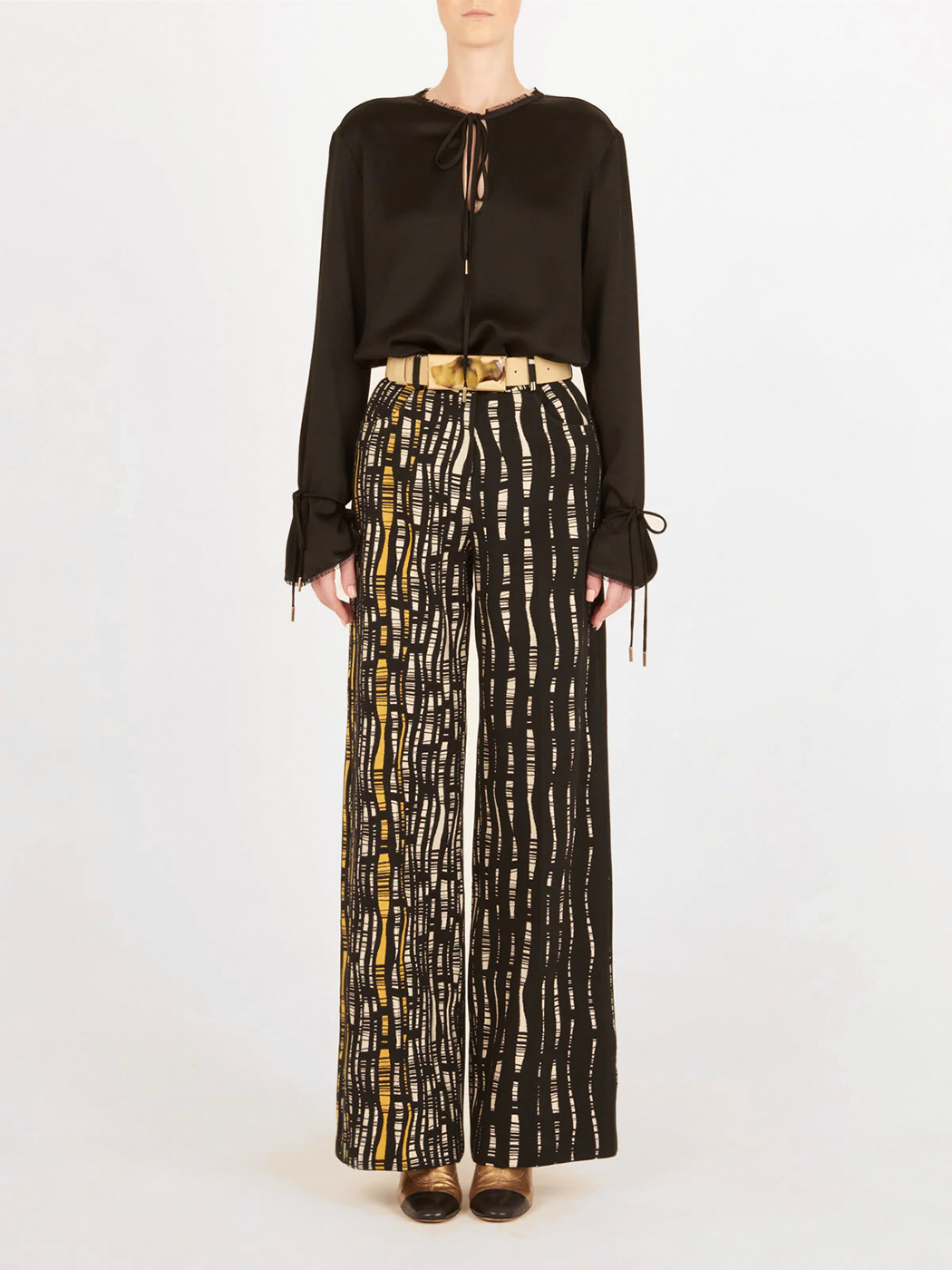 Emine Pant Black White: High-waisted, wide-leg pants with a black base and white and yellow abstract line pattern, shown against a plain white background.