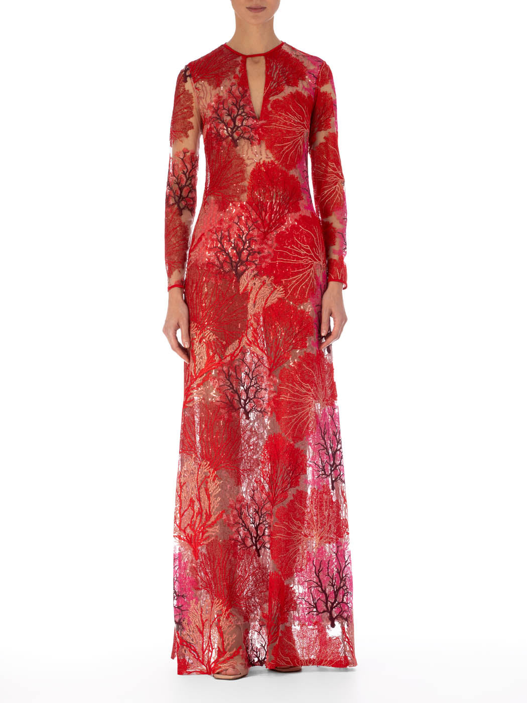 A person wearing the Enys Dress Multi Coral, a long maxi dress with intricate floral patterns and coral motifs, featuring a keyhole neckline, stands against a plain white background.