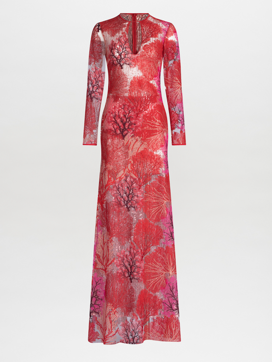 A person wearing the Enys Dress Multi Coral, a long maxi dress with intricate floral patterns and coral motifs, featuring a keyhole neckline, stands against a plain white background.