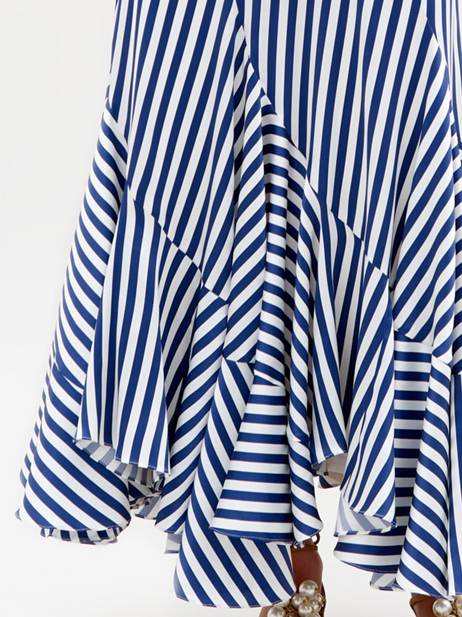 Against a plain background, a person is wearing the Florina Skirt, featuring long blue and white stripes with a deep V-neck, tie front, and ruffled hemline.